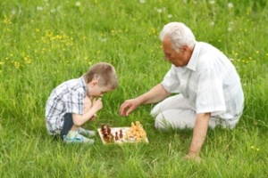 Grandfather and grandson playing chess on the grass in the meadow