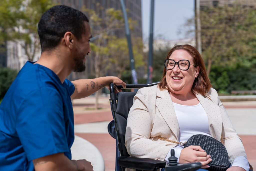 Nurse assisting a cheerful woman in a wheelchair outdoors
